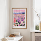 a framed poster of a colorful field of flowers hanging on a wall, with mountains visible in the background.