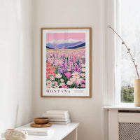 a framed poster of a colorful field of flowers hanging on a wall, with mountains visible in the background.