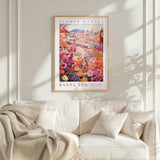 a framed poster of a colorful flower market scene hanging on a wall above a white couch with a blanket draped over it.