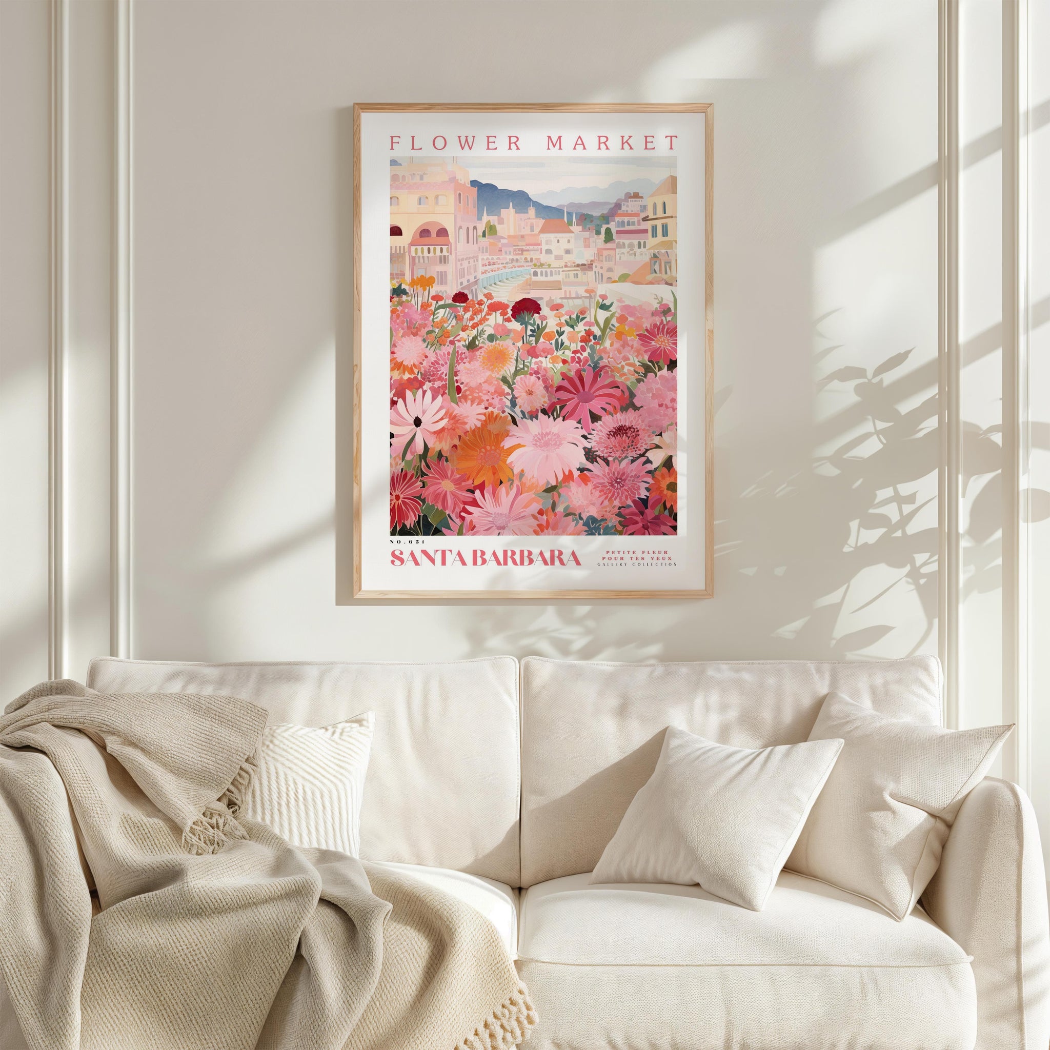 a framed poster of a colorful floral scene hanging on a wall above a white couch with a blanket draped over it.