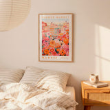 a bedroom scene with a framed poster of a colorful floral market hanging on the wall above a bed with striped pillows.