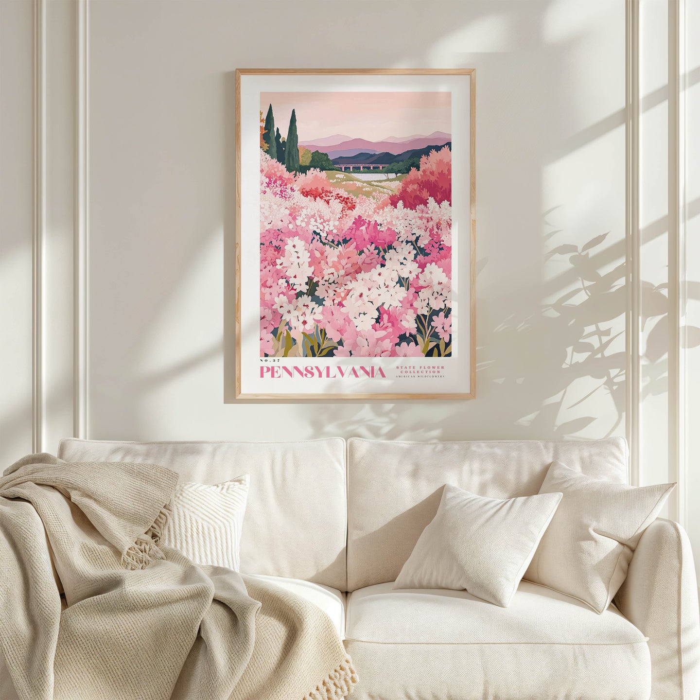 a framed poster of a field of pink flowers hanging on a wall above a white couch with a blanket draped over it.