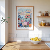 a kitchen scene with a framed poster of a colorful flower market on the wall, a wooden counter with a bowl of lemons, and shelves displaying various jars and containers.