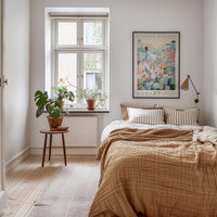 a cozy bedroom with a large bed, a wooden nightstand, and a window with a plant on the sill. The room has a neutral color scheme with a brown blanket and a wooden floor.