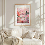 a framed poster of a pink and white floral scene hanging on a white wall above a white couch with a blanket draped over it.