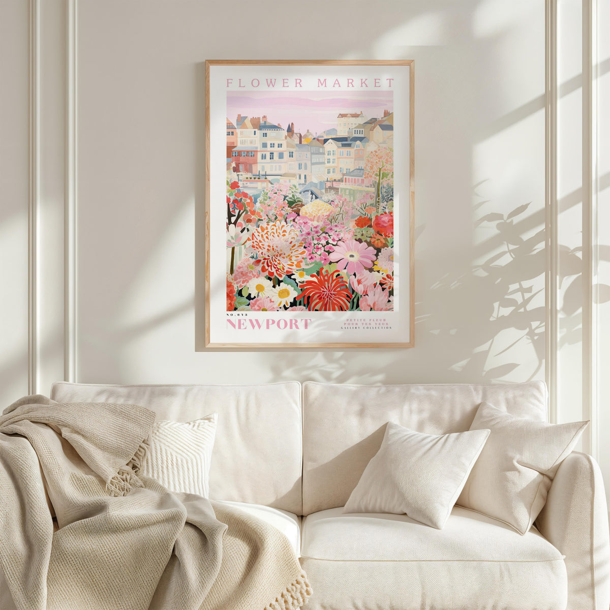 a framed poster of a colorful garden scene hanging on a wall above a white couch with a blanket draped over it.