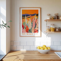 a framed poster of a colorful garden scene with flowers, hanging on a wall above a wooden countertop with a bowl of lemons.
