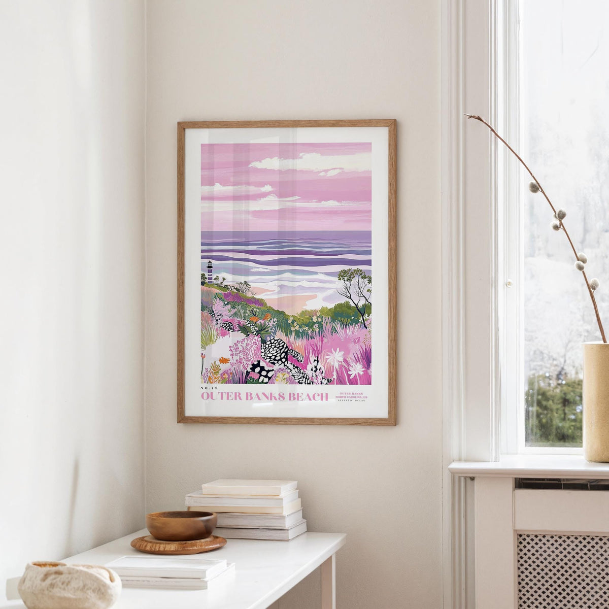 a framed poster of a beach scene with a colorful, abstract landscape, hanging on a wall in a room with a white table and a window.