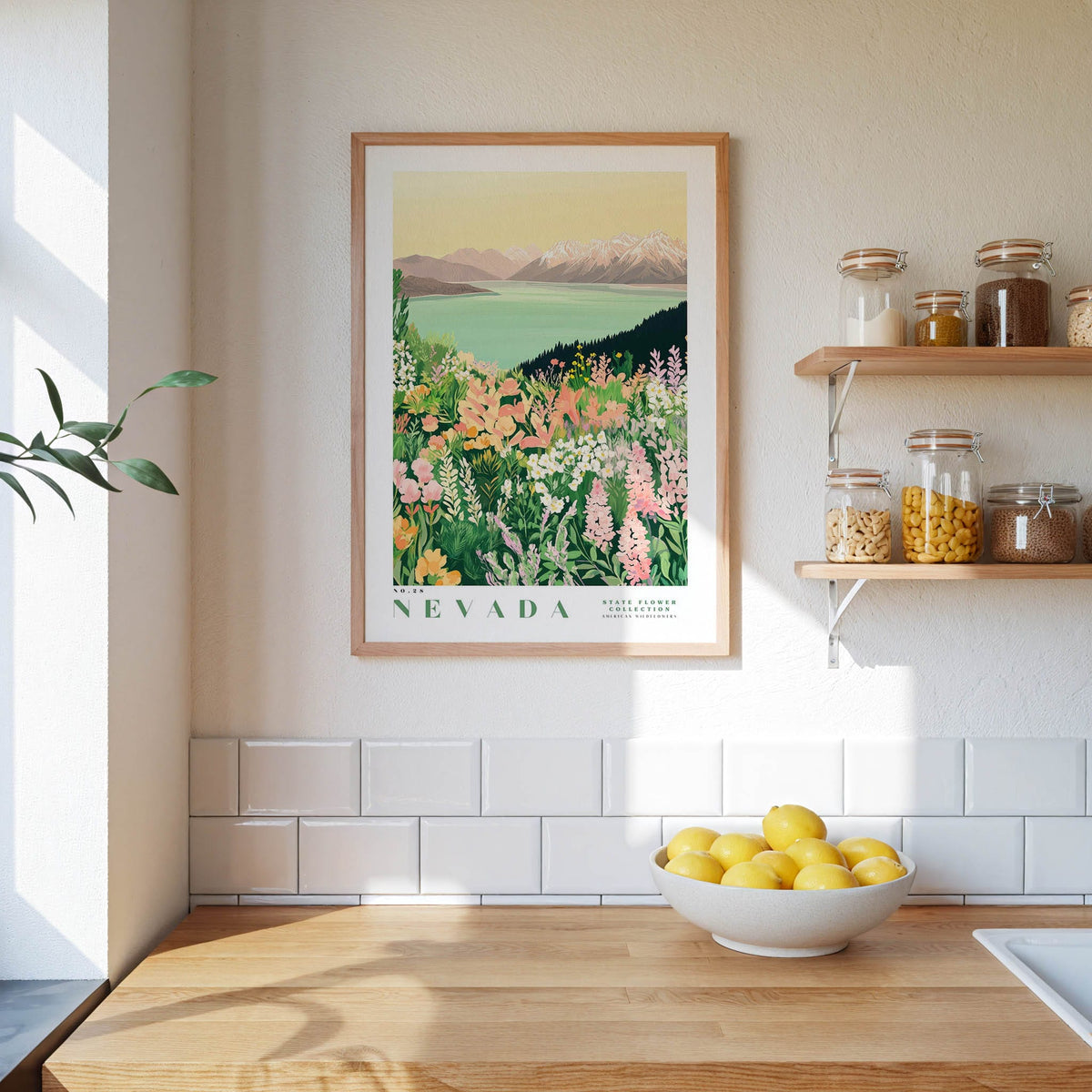 a kitchen scene with a framed print of a colorful landscape of flowers and mountains hanging on the wall above a wooden countertop. On the countertop, there is a bowl of lemons and a plant, and a shelf with various jars and containers.