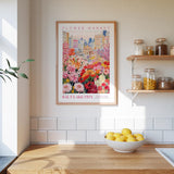 a framed poster of a colorful cityscape with flowers, hanging on a wall above a wooden counter with a bowl of lemons.