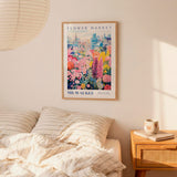 a bedroom setting with a framed poster of a colorful floral scene hanging on the wall above a bed with striped pillows.