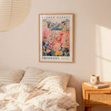 a bedroom setting with a framed poster of a colorful garden hanging on the wall above a bed with striped pillows.