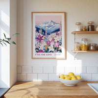 a framed poster of a mountain landscape with a variety of flowers, hanging on a wall above a wooden countertop with a bowl of lemons.