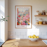 a kitchen scene with a framed poster of a flower market in Alexandria hanging on the wall above a wooden counter. On the counter, there is a bowl of lemons and a plant.