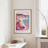 a framed poster of Key West Beach hanging on a wall, with a window and a small table with books and a vase in the foreground.