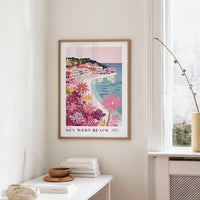 a framed poster of Key West Beach hanging on a wall, with a window and a small table with books and a vase in the foreground.
