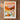 The image is a framed poster depicting a scenic landscape with mountains, flowers, and a warm, orange sky.