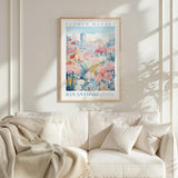 a framed poster of a cityscape with a flower market in the background, hanging on a wall above a white couch with a blanket draped over it.