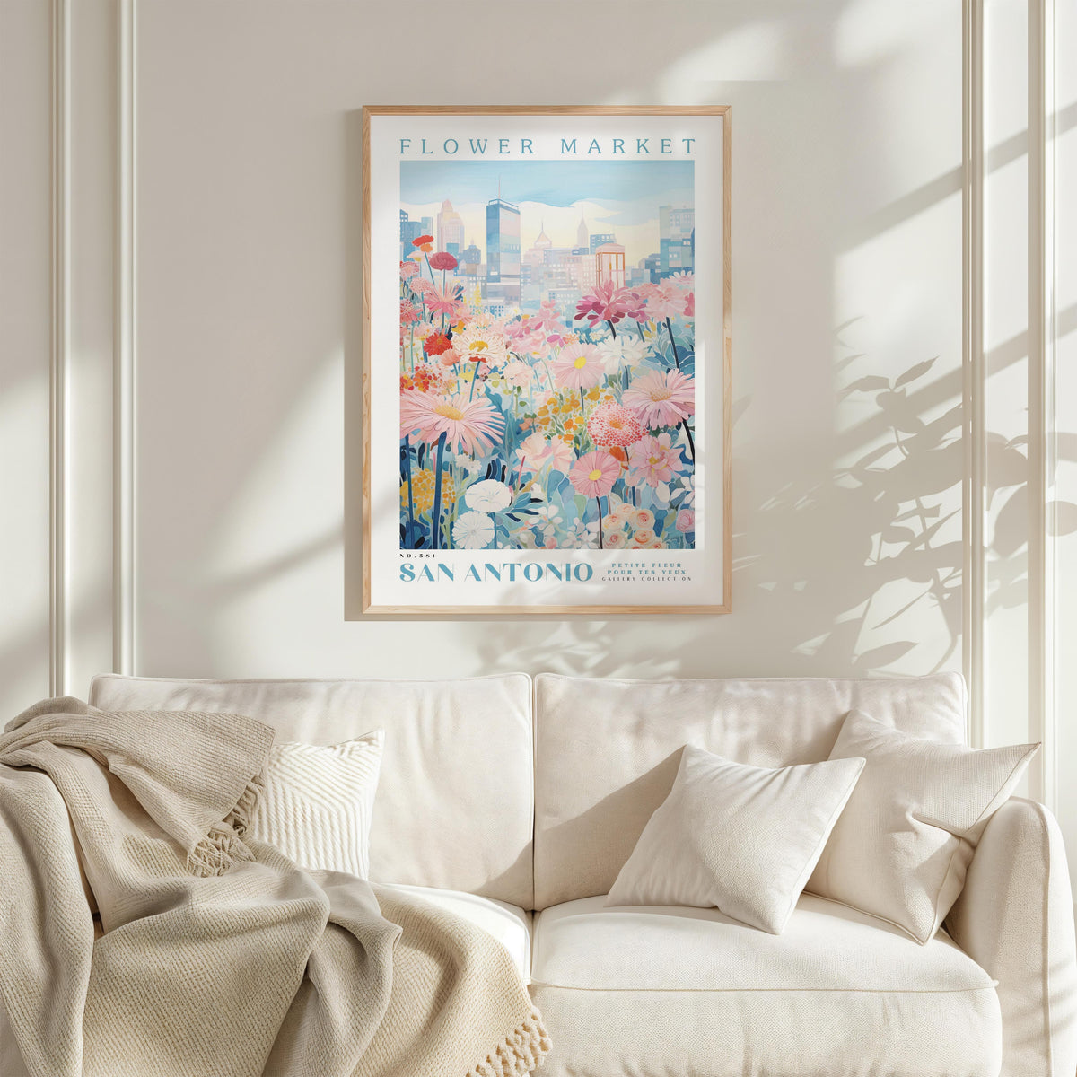 a framed poster of a cityscape with a flower market in the background, hanging on a wall above a white couch with a blanket draped over it.