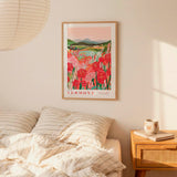 a bedroom scene with a framed poster of a field of flowers hanging on the wall above a bed with striped pillows.