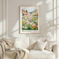 a framed poster of a flower market in Monterey, California, hanging on a wall above a white couch with a blanket draped over it.
