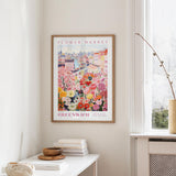 a framed poster of a colorful floral scene hanging on a wall, with a white table and a vase of flowers nearby.