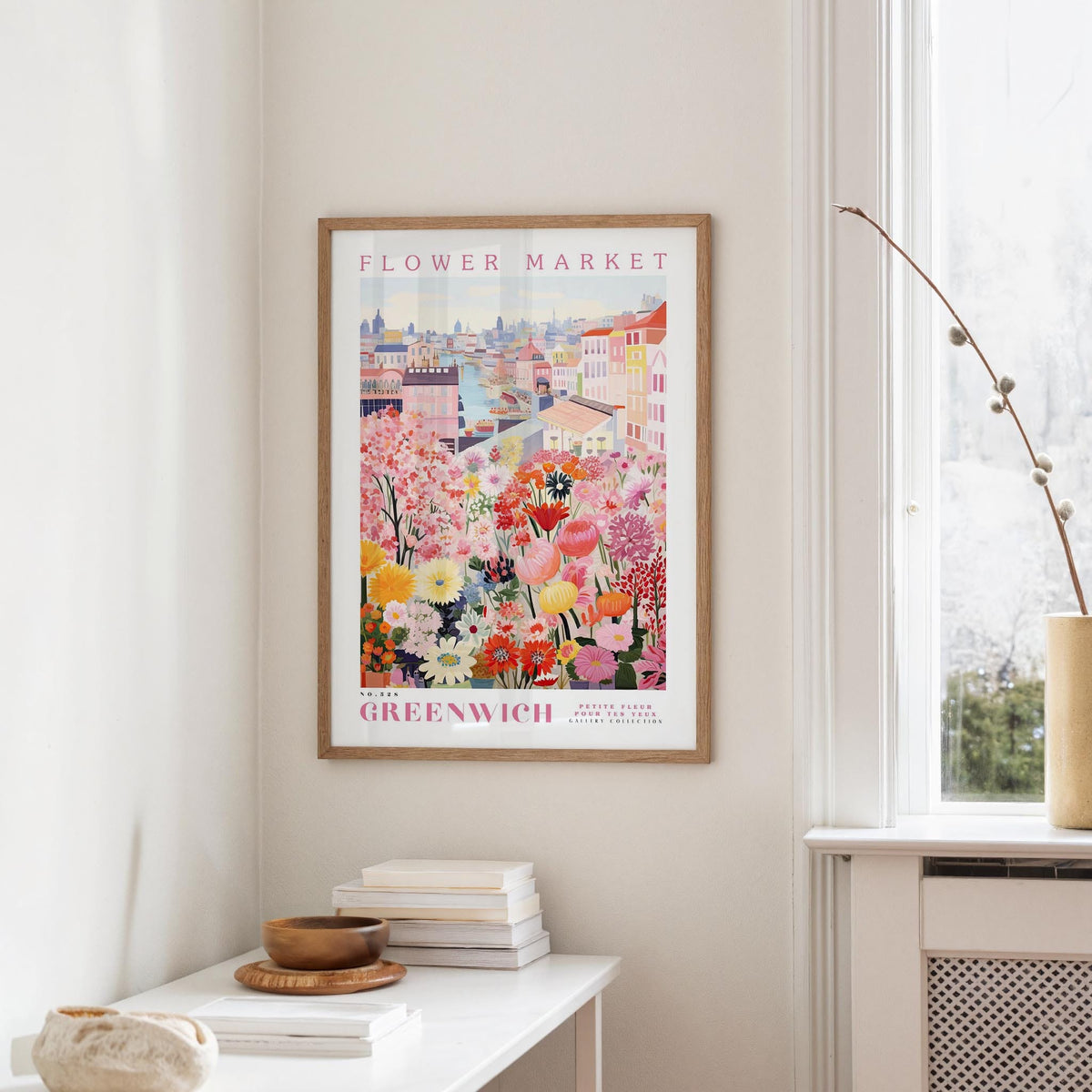 a framed poster of a colorful floral scene hanging on a wall, with a white table and a vase of flowers nearby.