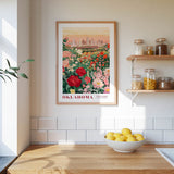 a framed poster of a garden with flowers hanging on a wall above a wooden countertop with a bowl of lemons.