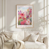 a framed poster of a vibrant floral scene hanging on a wall above a white couch with a blanket draped over it.