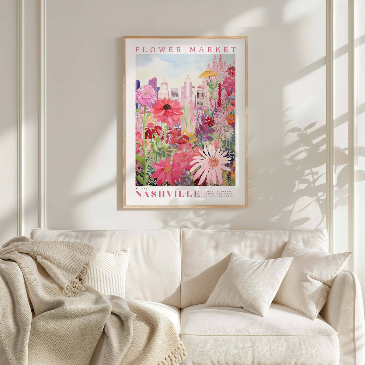 a framed poster of a vibrant floral scene hanging on a wall above a white couch with a blanket draped over it.