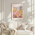 a framed poster of a cityscape with a field of flowers in the foreground, hanging on a wall above a white couch with pillows.