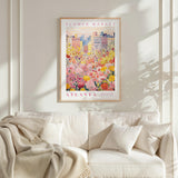 a framed poster of a cityscape with a field of flowers in the foreground, hanging on a wall above a white couch with pillows.