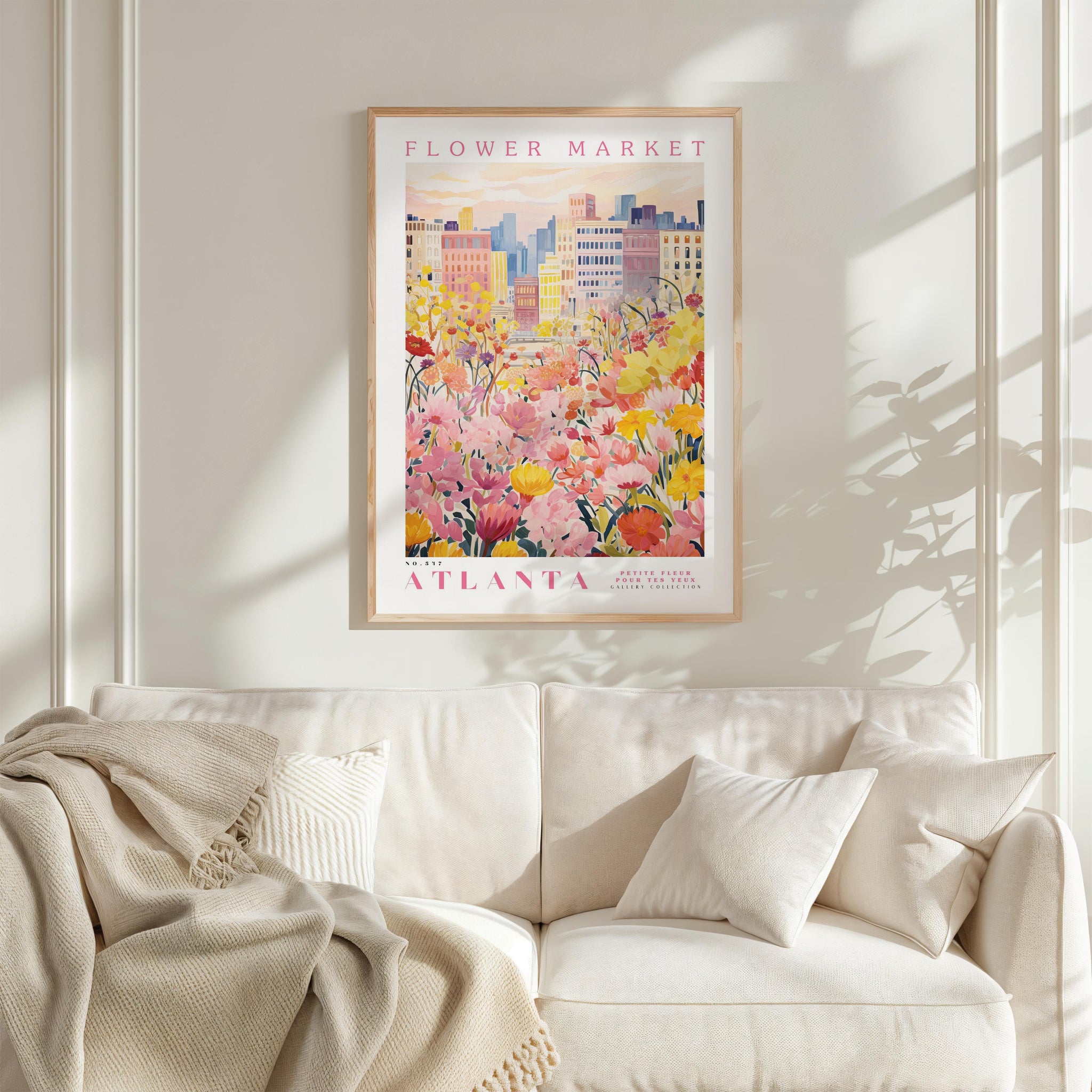 a framed poster of a cityscape with a field of flowers in the foreground, hanging on a wall above a white couch with pillows.