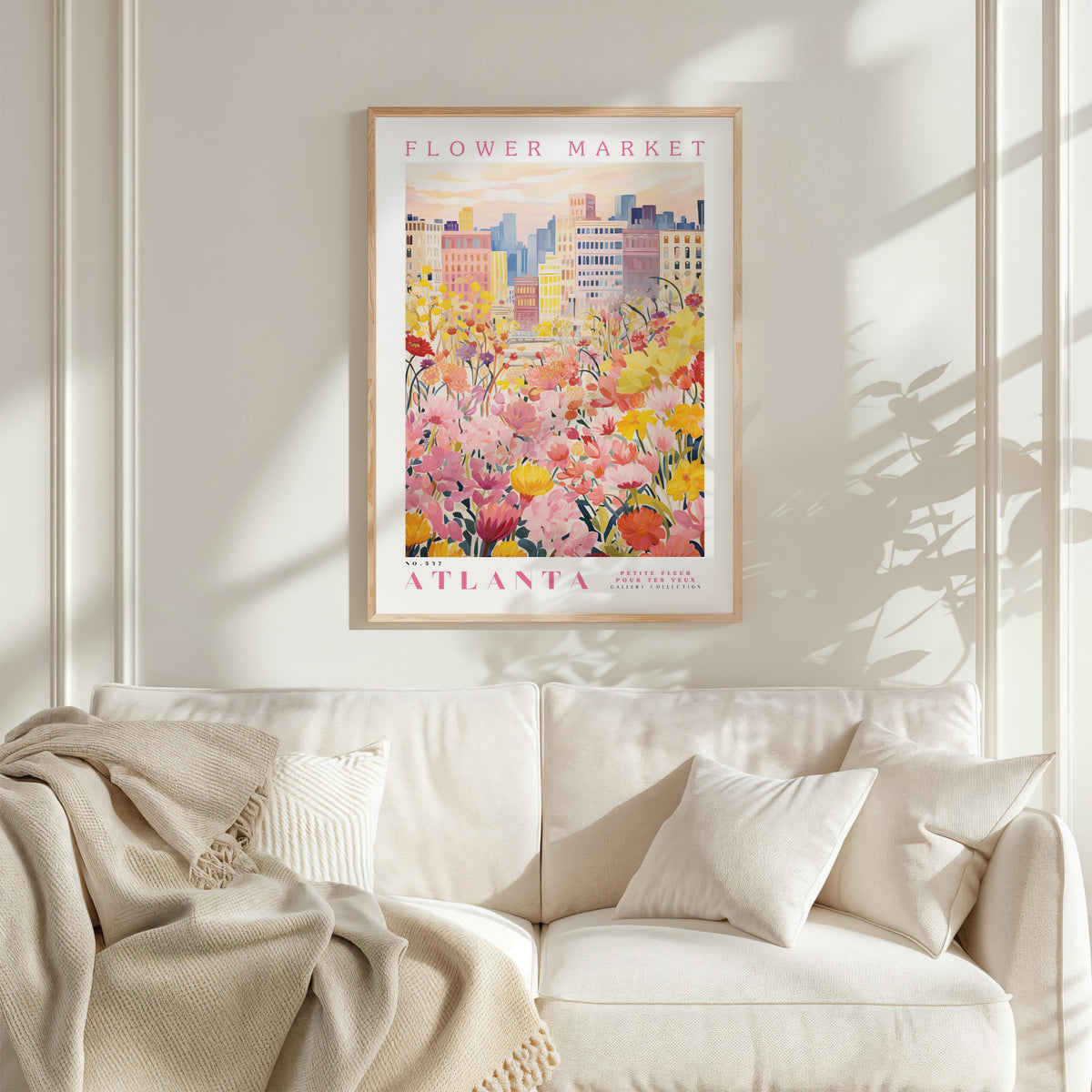 a framed poster of a cityscape with a field of flowers in the foreground, hanging on a wall above a white couch with pillows.