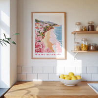 a framed poster of a beach scene with a wooden frame, hanging on a wall above a kitchen counter with a bowl of lemons and jars of food on the counter.