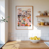 a kitchen scene with a framed poster of a flower market in Wilmington, Australia, hanging on the wall above a wooden counter. The poster displays a variety of colorful flowers and plants, creating a vibrant and lively atmosphere. On the counter, there is a bowl of lemons, adding a touch of freshness to the scene. The overall composition of the image is visually appealing and showcases the beauty of the flower market in Wilmington.