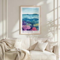 a framed poster of a vibrant underwater scene, with a lush coral reef and a serene ocean backdrop. The poster is hung on a white wall above a beige couch, which is adorned with a throw blanket and a single pillow.