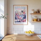 a framed poster of Melbourne's Flower Market, with a wooden shelf below it holding various jars and containers. A bowl of lemons is placed on a wooden countertop, and the kitchen has white tiled walls.