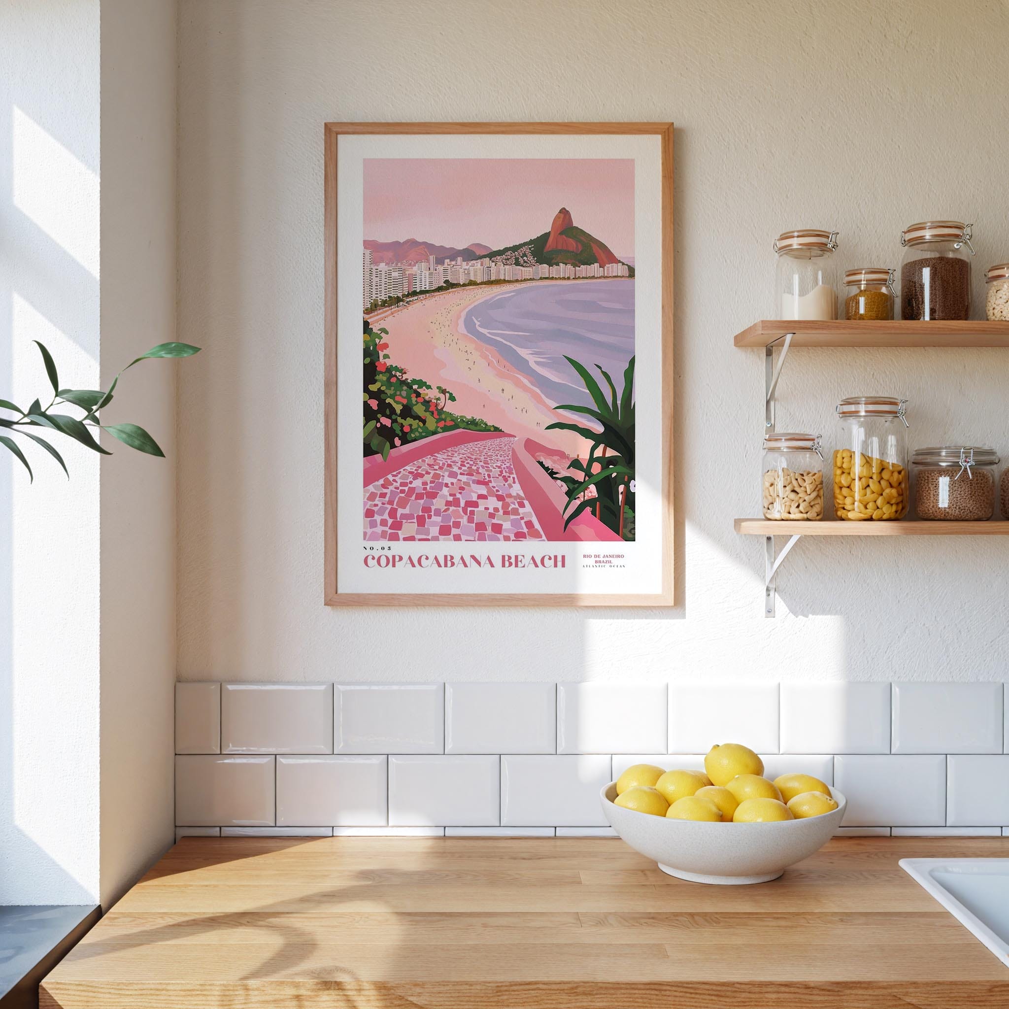 a framed poster of Copacabana Beach hanging on a wall above a kitchen counter with a bowl of lemons on it.