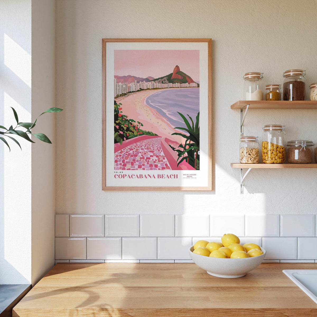 a framed poster of Copacabana Beach hanging on a wall above a kitchen counter with a bowl of lemons on it.