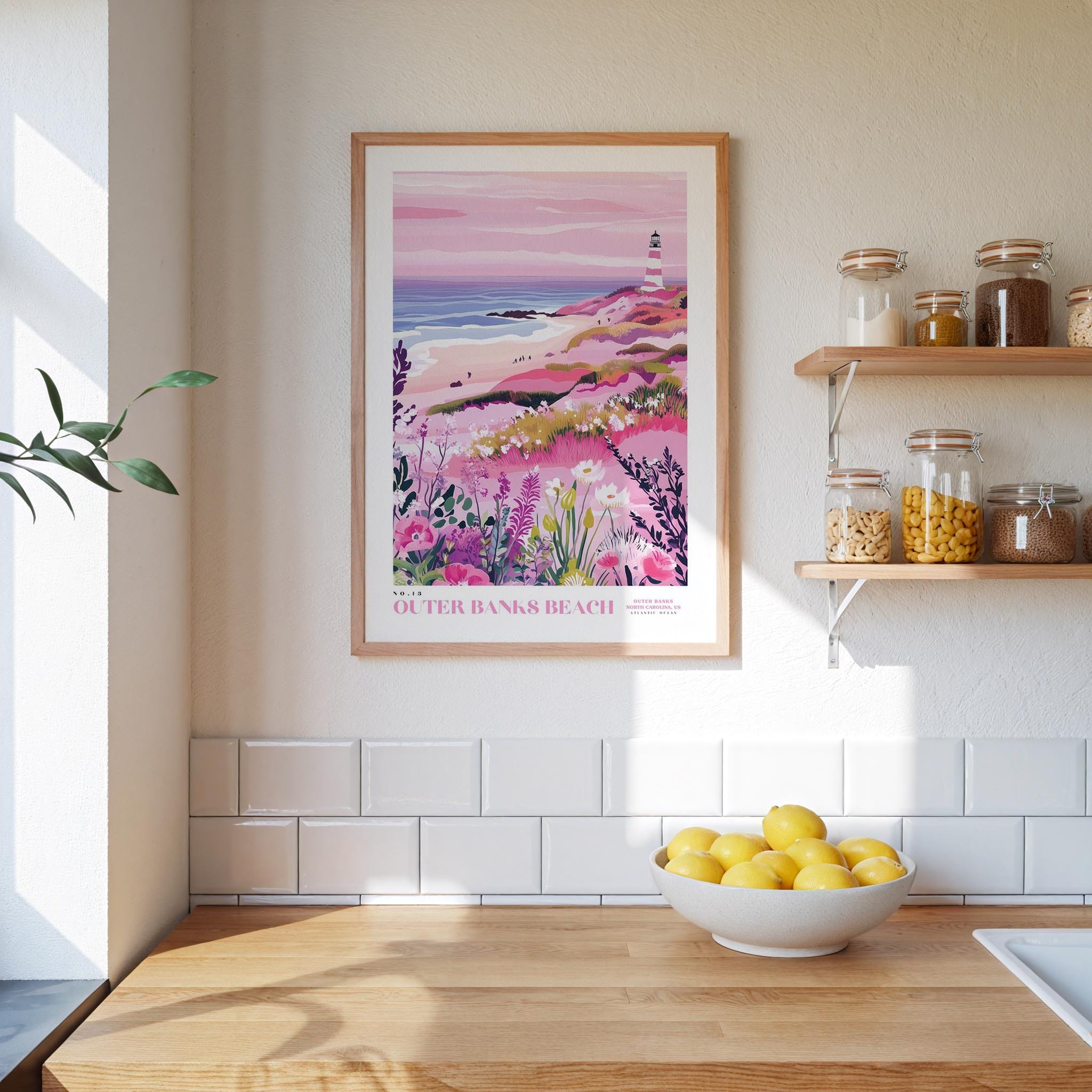 a kitchen counter with a bowl of lemons, a framed poster of a coastal landscape, and a shelf with jars and bottles.