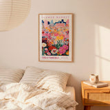 a bedroom setting with a framed poster of a colorful floral scene hanging on the wall above a bed with striped pillows.