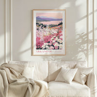 a framed poster of a scenic landscape with a lake and mountains, hanging on a wall above a white couch with a blanket draped over it.