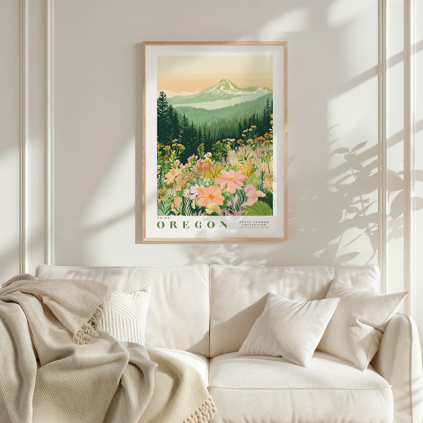 a framed poster of a mountain landscape with flowers hanging on a wall above a white couch with a blanket draped over it.
