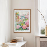 a framed poster of a colorful garden scene hanging on a wall, with a window and a small table with books and a vase nearby.
