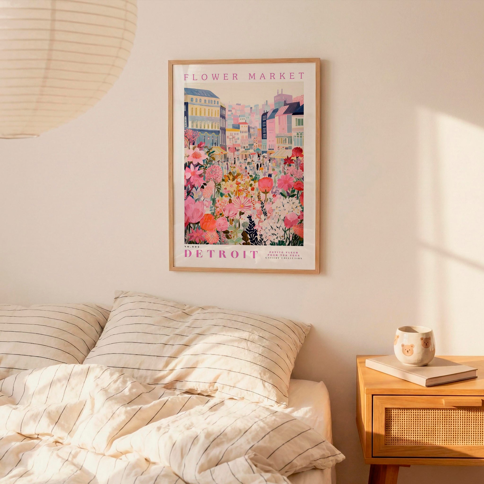 a framed poster of a colorful cityscape with flowers hanging on a wall above a bed with striped pillows.