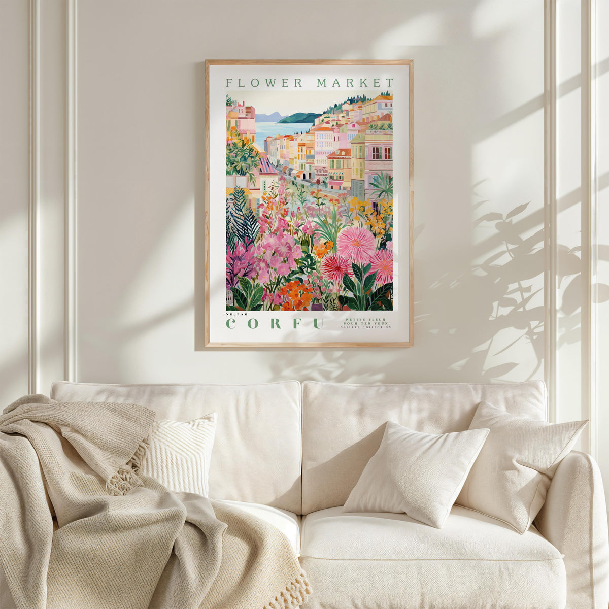 a framed poster of a colorful floral scene hanging on a wall above a white couch with a blanket draped over it.