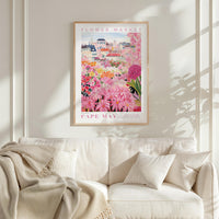 a framed poster of a colorful floral scene hanging on a wall above a white couch with a blanket draped over it.