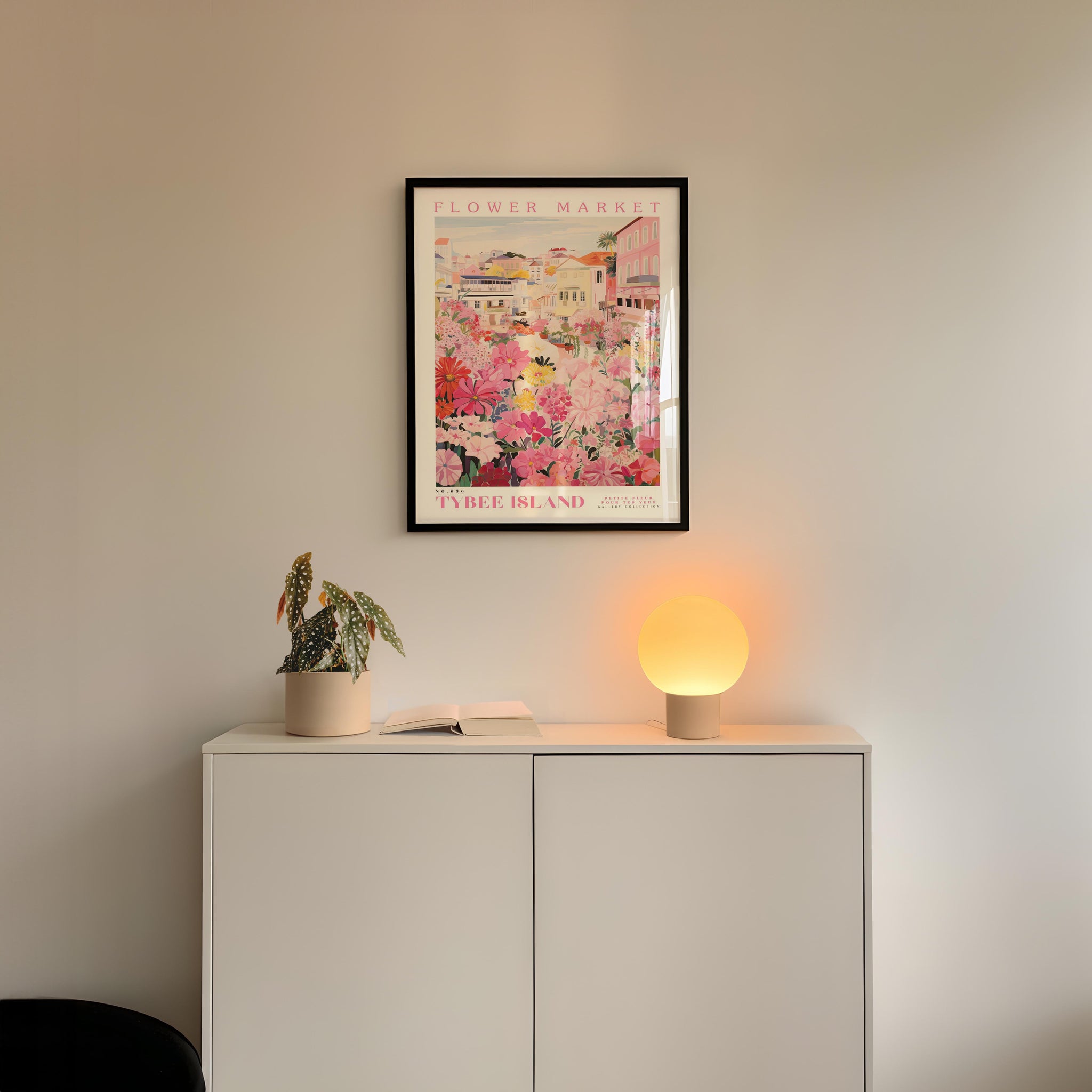a white cabinet with a potted plant and a lamp on top, set against a wall with a framed poster of a flower market in the background.