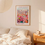 a bedroom scene with a framed poster of a colorful flower market hanging on the wall above a bed with striped bedding.